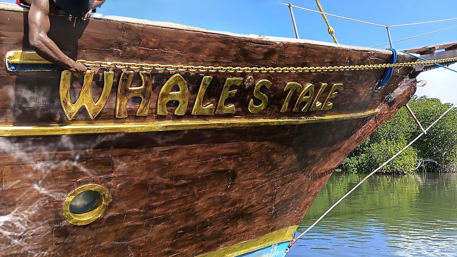 Close-up of the gold Whale's Tale lettering and gold chain detail on the ship's timber bow