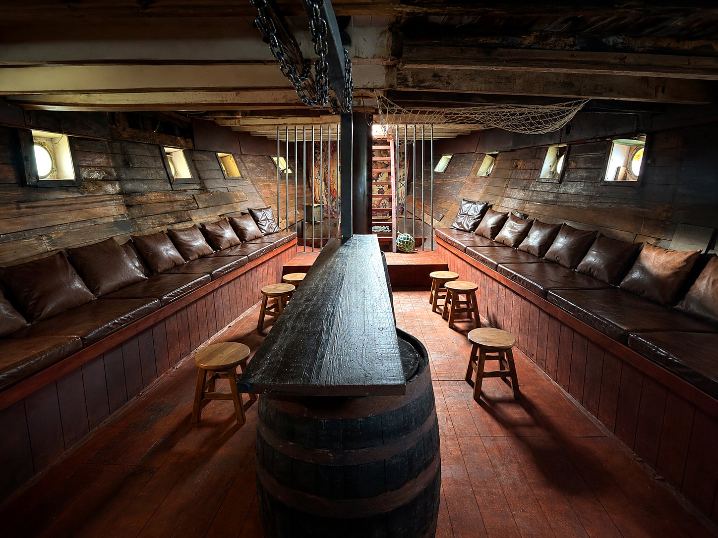 The Kraken's Hold below deck: long leather bench seating along both curved timber hulls with a barrel bar down the centre